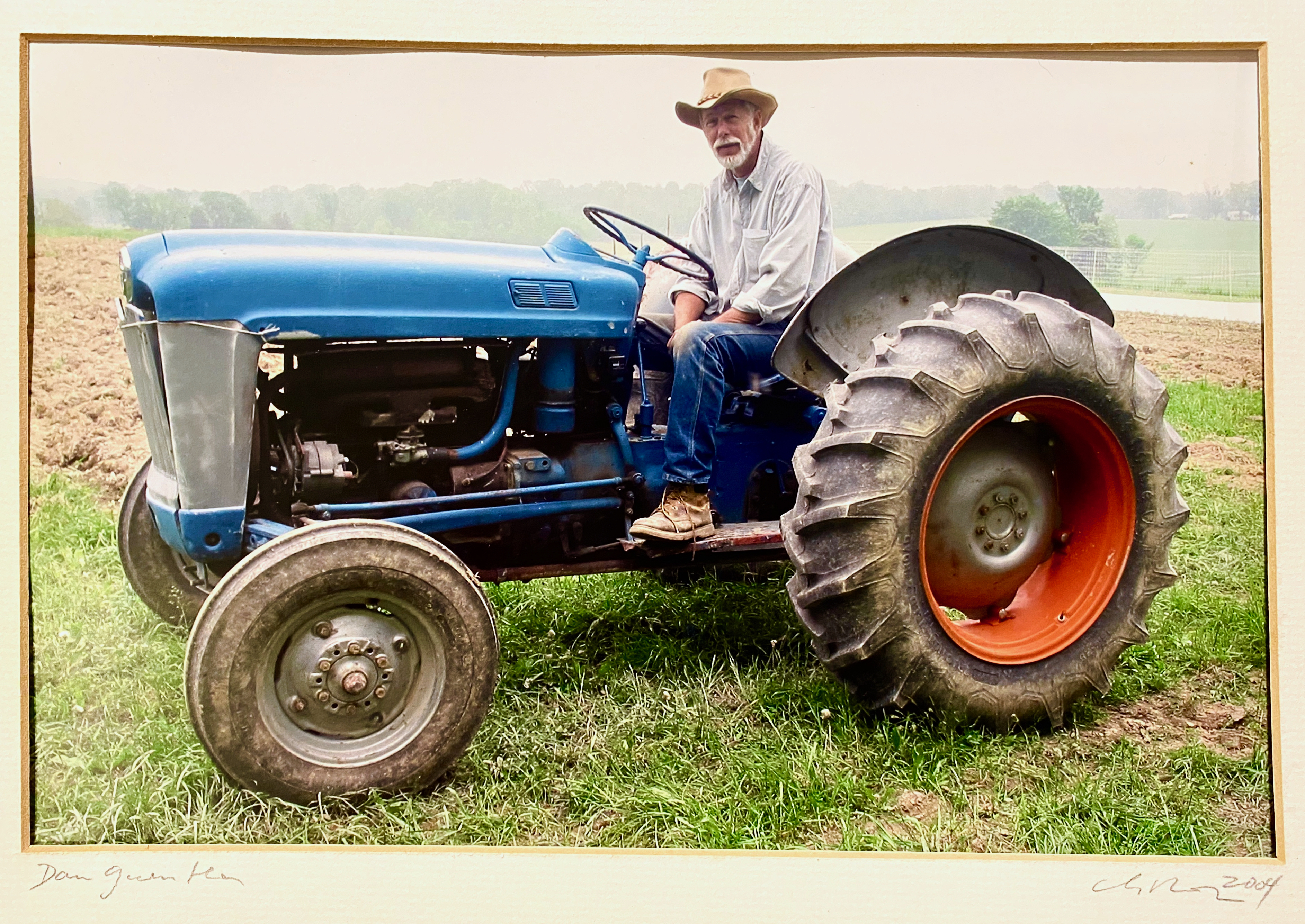 Dan Guenther, a bearded, white-haired man on a blue tractor in a field at Phillies Bridge Farm CSA.